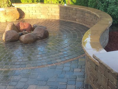 Patio designed with a stone fire pit and stone seating wall.