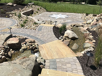 Landscaping lighting illuminates a brick and stone path and a custom patio design.